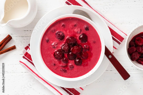 Fototapeta Sour cherry soup in a white bowl on a white background. Top view. Hungarian cold cherry soup with cream or sour cream, sugar and cinnamon. Sweet summer soup.