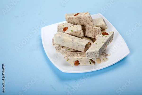 Fototapeta Halva with pistachios and almonds is on a white porcelain plate against a blue background.