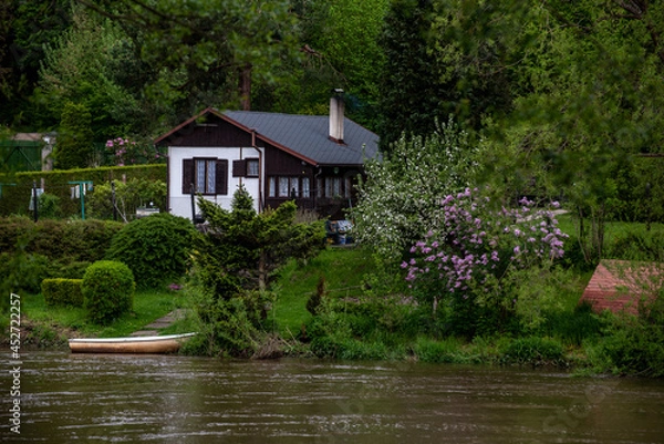 Fototapeta cottage on the river bank and a boat in front of it