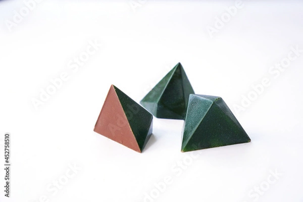 Fototapeta Luxury pyramid shaped chocolate candy. Three chocolates - green color and geometric triangular candy design. Handmade work. Isolated sweets on white