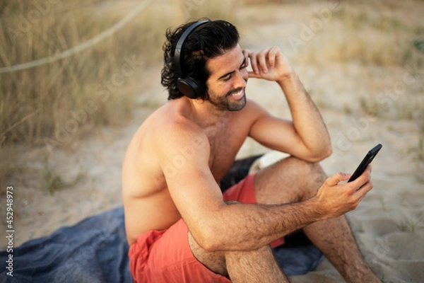 Obraz Young man sitting on the beach. Young man listening the music while relaxing at the beach