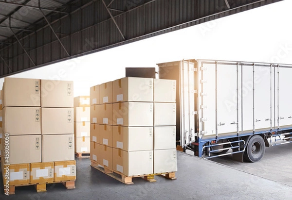 Fototapeta Packaging Boxes Stacked on Pallets Loading with Shipping Cargo Container. Truck Parked Loading at Dock Warehouse. Delivery. Warehouse Logistics. Cargo Freight Truck Transportation.	
