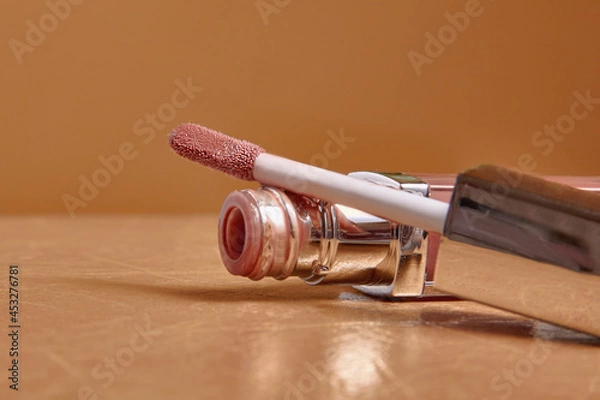 Fototapeta Liquid lipstick and applicator on  color background. Open tube of lip gloss and wand brush with makeup product on pastel surface. copy space