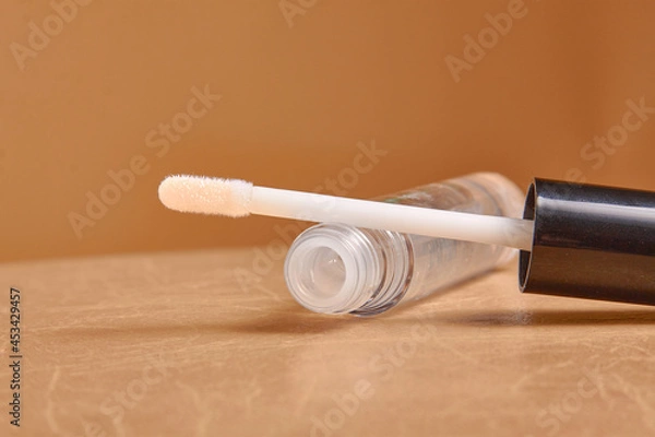 Fototapeta Liquid lipstick and applicator on  color background. Open tube of lip gloss and wand brush with makeup product on pastel surface. copy space
