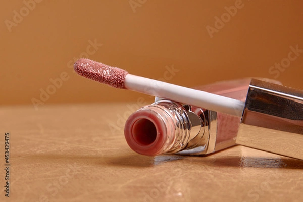 Fototapeta Liquid lipstick and applicator on  color background. Open tube of lip gloss and wand brush with makeup product on pastel surface. copy space