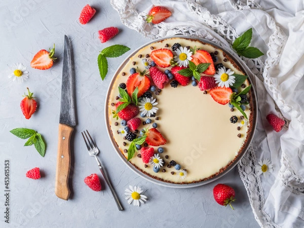 Fototapeta Cheesecake pie with fresh berries, strawberries, blueberries and blackberries and mint chamomiles in a round plate on a grey background.