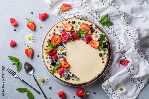 Fototapeta Cheesecake pie with fresh berries, strawberries, blueberries and blackberries and mint chamomiles in a round plate on a grey background.