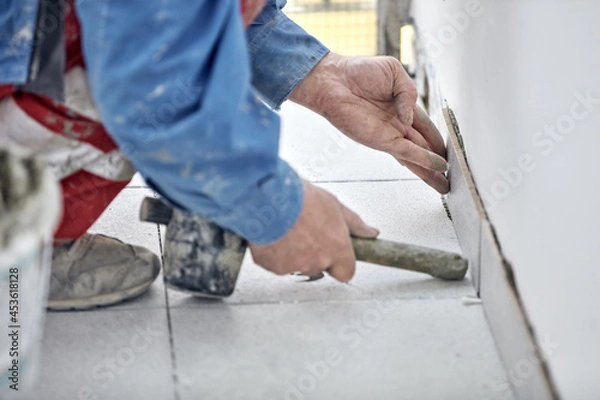 Fototapeta Ceramics tile man worker placing new tiles on the floor and wall.