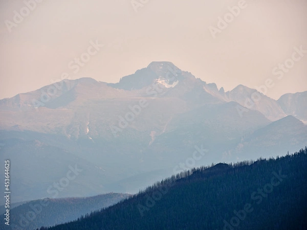 Fototapeta Rocky Mountains and forest trees shrouded in haze and smoke due to burning forest fires