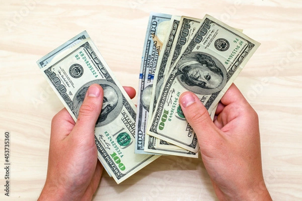 Obraz a man counts hundred-dollar bills sitting at a table