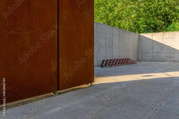 Fototapeta Wall made of architectural concrete and corten sheet surrounded by greenery in the park, a bicycle rack standing on a concrete floor