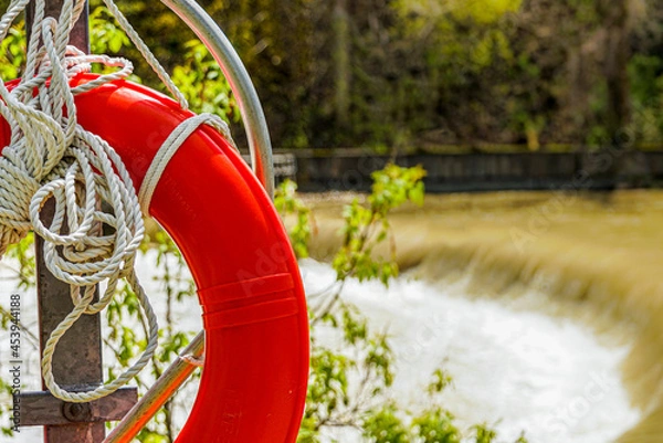Fototapeta lifebuoy, lifesaver to be thrown to a person in the water to rescue or prevent drowning, located on a pole at the edge of a  fast moving river.