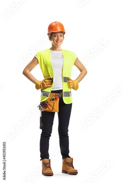 Fototapeta Full length portrait of a young female construction worker wearing a hardhat and a tool belt