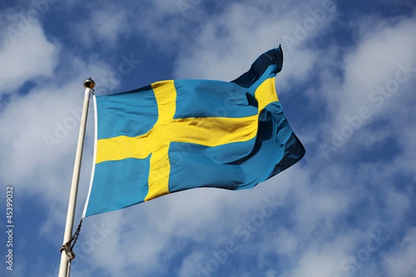 Obraz Waving swedish flag against blue sky with small white clouds