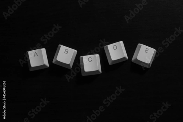 Fototapeta A,b,c,d,e alphabets letters on white keyboard keycaps on dark wood background, illustration.
