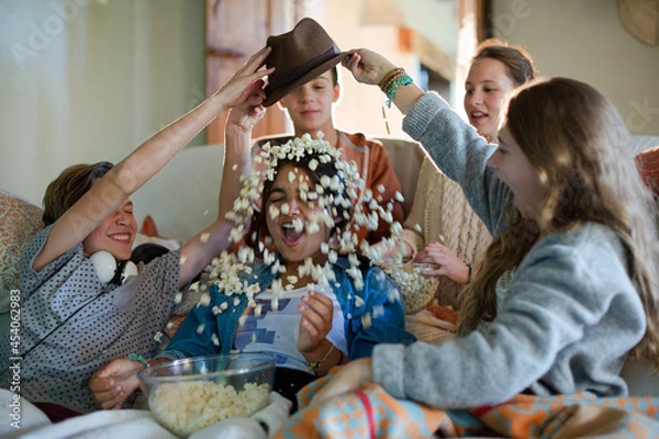 Fototapeta Group of teenagers throwing popcorn on themselves while sitting on sofa