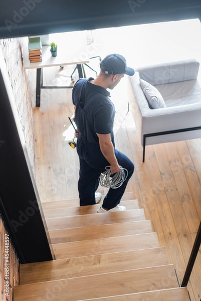 Fototapeta high angle view of workman with tools and wires walking downstairs in modern apartment