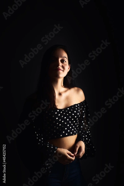 Fototapeta Half-length portrait of a young girl with a smile looking towards the camera, on a dark studio background