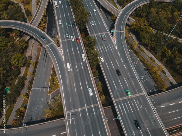 Fototapeta Top up aerial drone view of elevated road and traffic junctions in Chinese metropolis city during sunny day golden hour. Modern construction design of traffic ways to avoid traffic jams. Few vehicles.