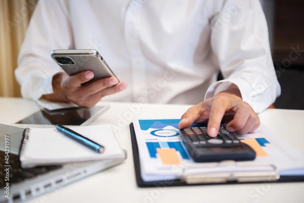 Fototapeta Investors are calculating on calculator investment costs and holding smartphone.