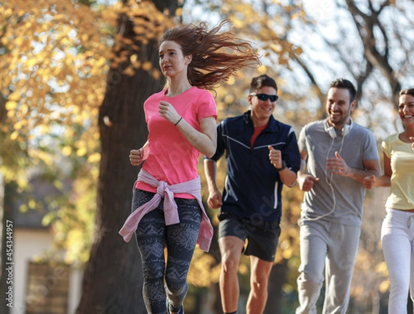 Fototapeta Red hair female in casual sport outfit jogging with her friends at city park.