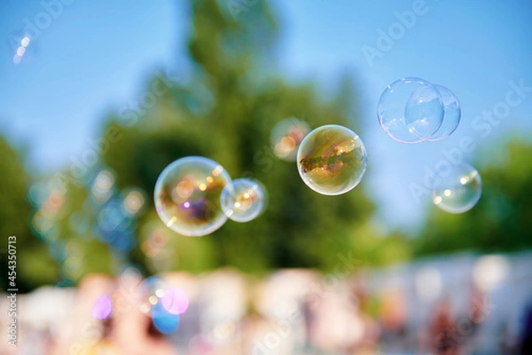 Fototapeta Beautiful soap bubbles at the park on a sunny day. A lot of bubbles in the air. Blurred background. Childhood concept photo. Large size image.