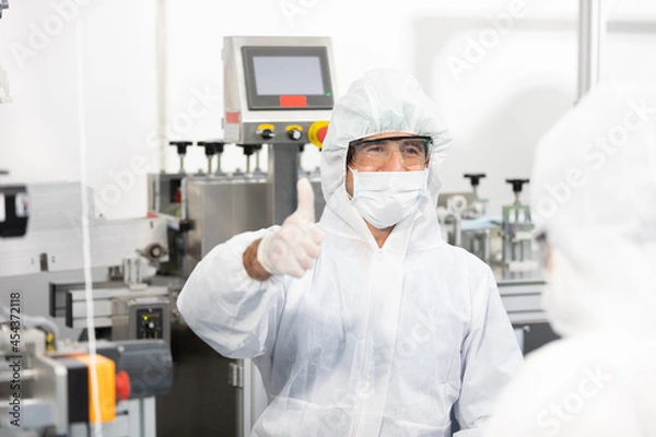 Fototapeta male engineers wearing personal protective equipment uniform(PPE) wearing medical face mask, producing medical face masks thumbs up pose beside machine in laboratory