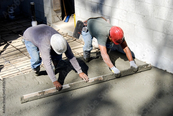 Fototapeta Masons using a screed to level freshly poured concrete