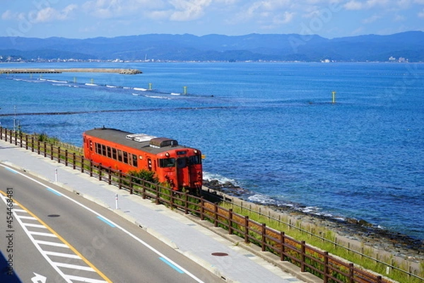 Obraz 海と空を背景に雨晴海岸の海沿いを走る氷見線の電車