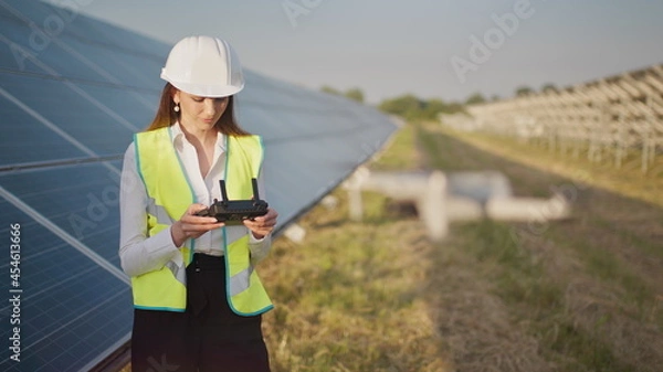 Fototapeta Portrait of a female engineer operating a drone on the background of a solar power plant. Solar panel array installation. Technologies and ecology. Sunsets.