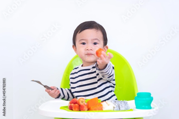 Fototapeta Happy Asian baby sitting in a children chair with fruit, healthy food concept.