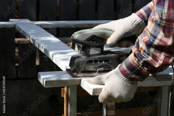 Fototapeta A man with an electric vibration sander treats the surface of a board