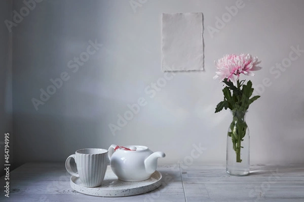Fototapeta Scandinavian style. Interior Design. Large pink chrysanthemum in a long glass vase. Cup and tea pot on the tray. Empty space for text