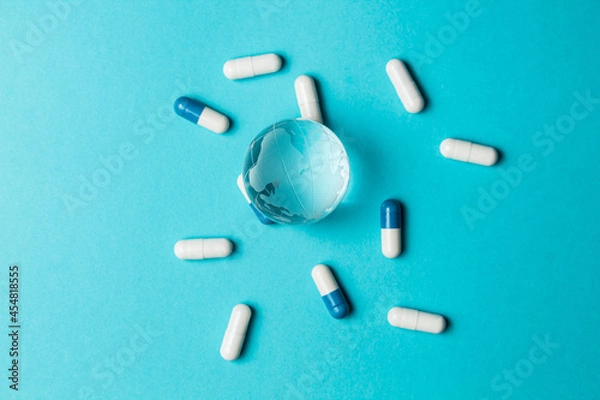 Fototapeta World pandemic. Global epidemic, pandemic concept. Glass globe Earth and capsule pill white-blue on a turquoise background. Medicine. Healthcare. Top view. Closeup