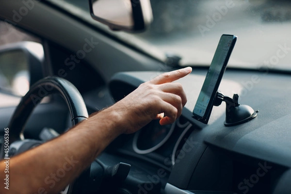 Fototapeta Navigator in car vehicle transportation commuter. Driver man pointing hand finger mobile phone navigator app while driving car.