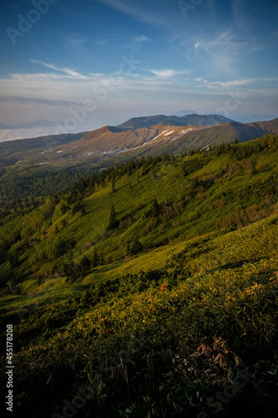 Obraz 朝の太陽に照らされて輝く峠の草原と山の向こうに青空が広がる