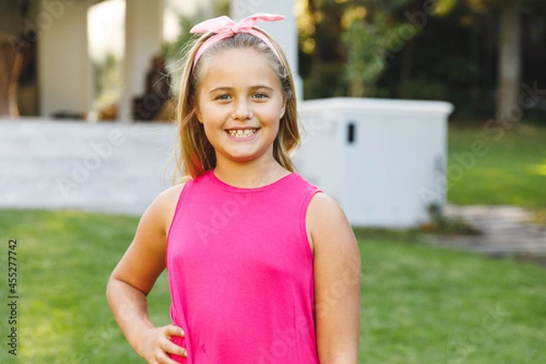 Fototapeta Portrait of smiling caucasian girl outside house looking at camera in garden