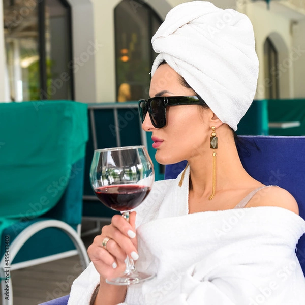 Fototapeta Young caucasian girl in a bathrobe and a towel relaxing with a glass of wine.
