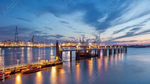 Obraz Pier in river Scheldt with container terminal on background at twilight, Port of Antwerp, Belgium.