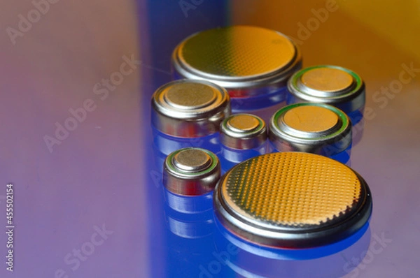 Obraz small button batteries of different sizes, highlighted in red and orange, lie against a blue background. close-up.