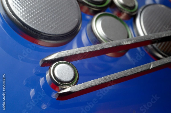 Fototapeta a small battery clamped with tweezers against the background of other small batteries. close-up.