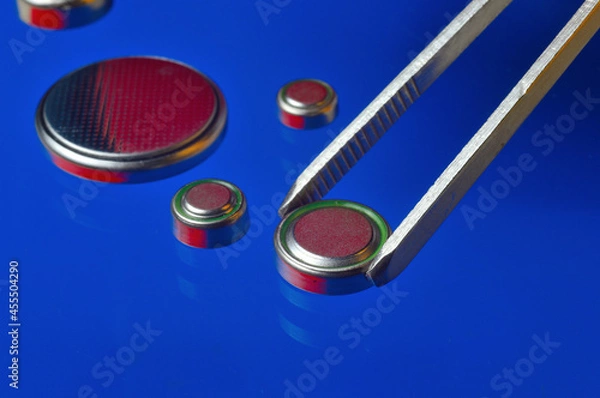 Fototapeta a small battery clamped with tweezers against the background of other small batteries. close-up.