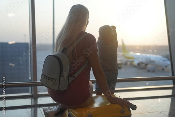 Fototapeta Mother and son sitting on a yellow suitcase at the airport and looking at the plane.
