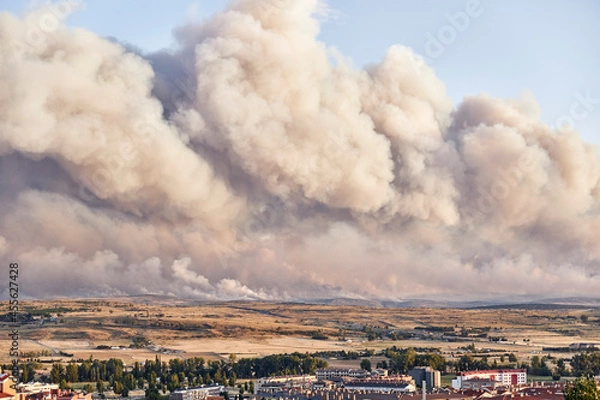 Fototapeta Photograph of a large forest fire with a large column of smoke on a hillside near a city