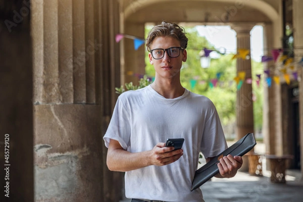 Obraz A man with a smartphone in his hands looks at the camera. Business young man wearing glasses with smartphone