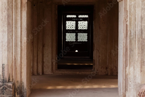 Fototapeta A beautifully carved lattice window casting light and shadow in a hall in the ancient Raja Mahal palace.