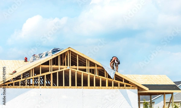 Fototapeta Worker installing on wooden roof of new house with couds blue sky. Renovation, improvement for exterior residential by professional builder. Durable build and construction business. Labor job concept