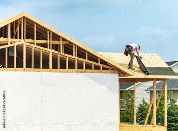 Fototapeta Worker installing underlayment sheet on wooden roof of new house. Renovation, improvement for exterior residential by professional builder. Durable build and construction business. Labor job concept