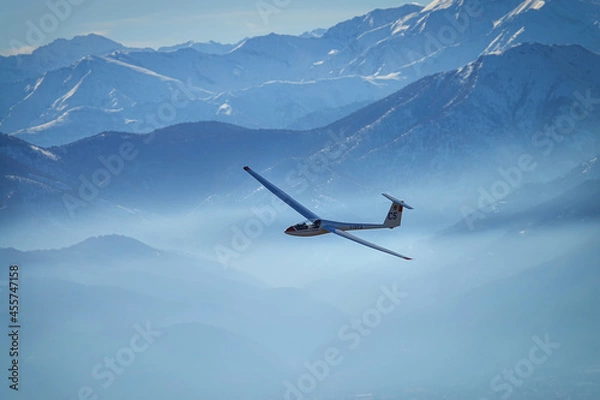 Fototapeta Glider in flight between snowy mountains seen from above. Susa, Italy - January 2021