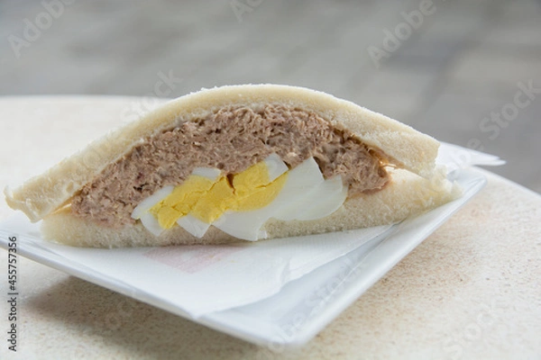 Fototapeta Close up of a Tramezzino, a triangular Italian sandwich constructed from two slices of soft white bread, with the crusts removed, containing hard boiled egg and tuba fish 